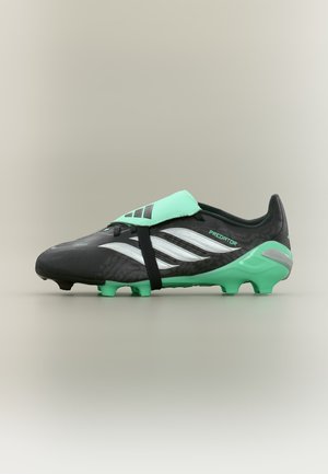 Chaussure de football Adidas Predator noire et verte avec des bandes argentées, une languette pliée et une semelle à crampons sur fond neutre.
