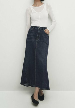 Dark denim maxi skirt with a high waist, front pockets, and subtle stitching details. Paired with a fitted white long-sleeve top.