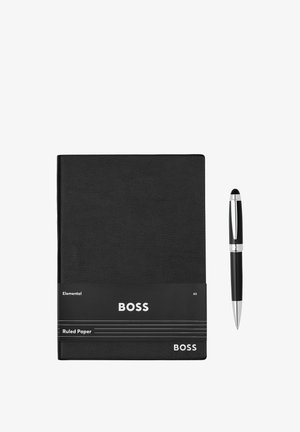 Carnet BOSS noir avec étiquette à papier ligné à côté d'un stylo à bille noir et argent sur fond blanc.