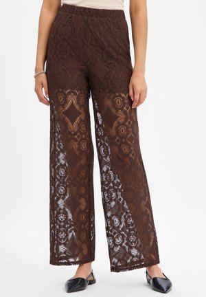 Bruine kanten brede pijpen broek met bloem- en geometrische patronen, gedragen met zwarte puntige platte schoenen en een wit topje.