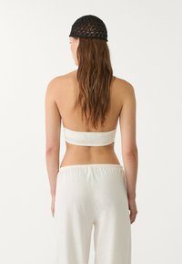 Hvid smocked bandeau-top parret med letvægts, løstsiddende hvide bukser; tekstureret sort strikket hat med et geometrisk mønster.