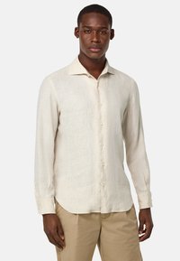 Camicia di lino beige chiaro con maniche lunghe, colletto a punta e chiusura con bottoni. Tessuto liscio e un sottile motivo a trama, abbinata a pantaloni khaki.