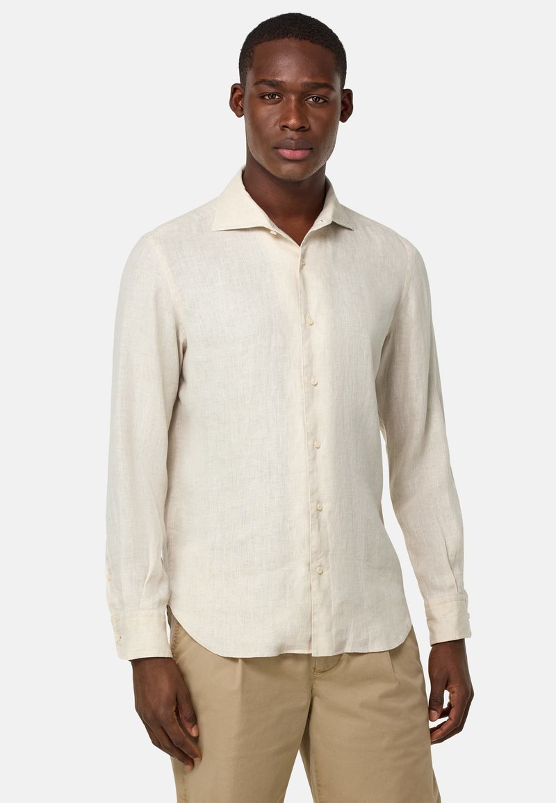 Camicia di lino beige chiaro con maniche lunghe, colletto a punta e chiusura con bottoni. Tessuto liscio e un sottile motivo a trama, abbinata a pantaloni khaki.