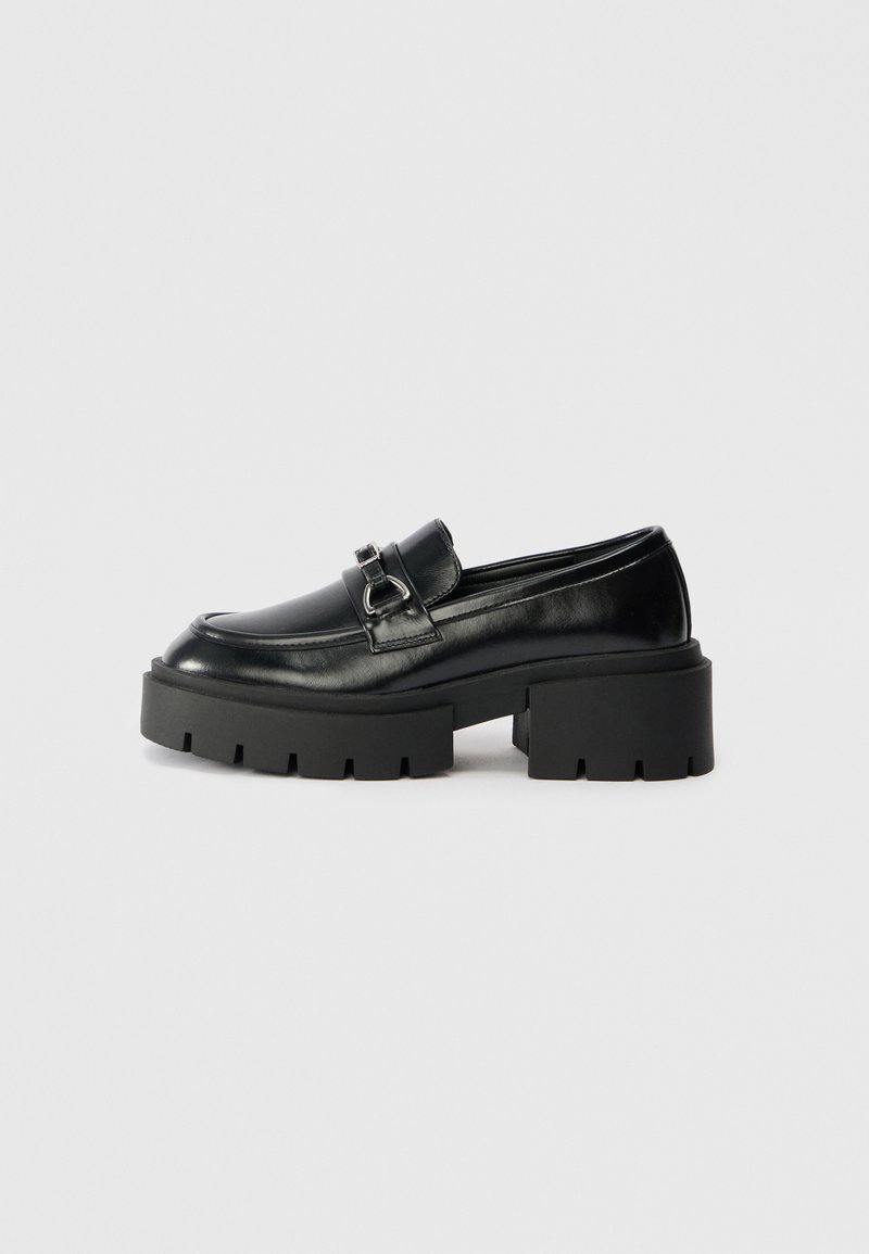 Black leather loafers with a rounded toe, chunky black sole, and metal buckle accent on the upper. Textured finish and sturdy design.