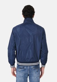 Giacca bomber blu navy realizzata in materiale leggero, con colletto alto e polsini elasticizzati, caratterizzata da accenti bianchi a righe sull'orlo.