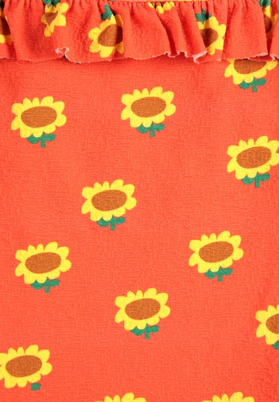 Tissu rouge avec une finition texturée, présentant un motif de tournesols jaunes avec des cœurs marron et des feuilles vertes, bordé d'un bord froncé.
