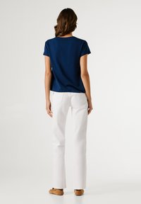 Μπλουζάκι από βαμβάκι σε ναυτικό μπλε χρώμα με κοντά μανίκια, συνδυασμένο με άσπρο παντελόνι. Το μοντέλο είναι γυρισμένο με την πλάτη, παρουσιάζοντας ένα απλό σχέδιο και άνετη εφαρμογή.