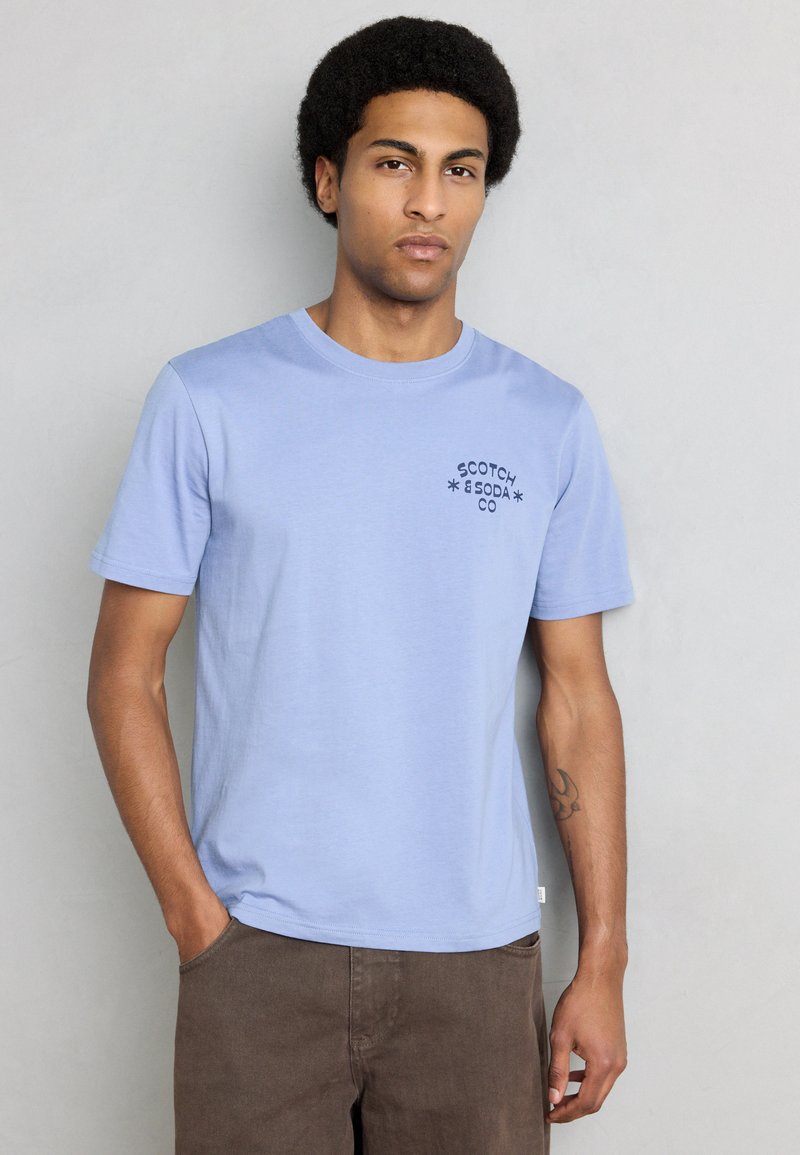 Ανοιχτό μπλε βαμβακερό T-shirt με στρογγυλό λαιμό και κοντά μανίκια, με ένα μικρό μαύρο λογότυπο στο αριστερό στήθος.