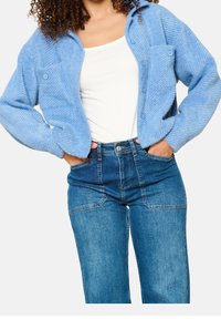 Světle modrý textura cardigan s zapínáním na knoflíky a dvěma předními kapsami, zkombinovaný s džínami s vysokým pasem v tmavě modré barvě.