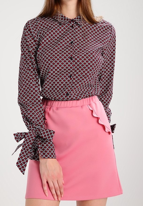 Röd och vit prickig skjorta med knäppning och bandknutna ärmar; parat med en rosa volangkjol i mini-längd.