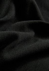 Tejido negro acanalado con una superficie texturizada, que presenta líneas diagonales sutiles y pliegues suaves, enfatizando su naturaleza suave y flexible.