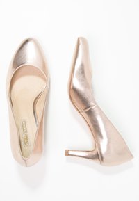 Roséguld högklackade skor med en glänsande metallisk finish, rund tå och en slät yta, med en avsmalnande klack och vadderad innersula.
