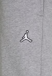 Grå mjukisbyxor i mjukt tyg med en svart och vit broderad Jumpman-logga på vänster sida. Enkelt design, inga mönster.