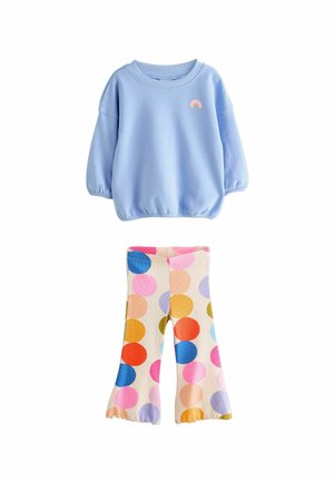 Felpa azzurro chiaro con polsini elasticizzati e una patch arcobaleno, abbinata a leggings crema con punti multicolori di varie dimensioni.