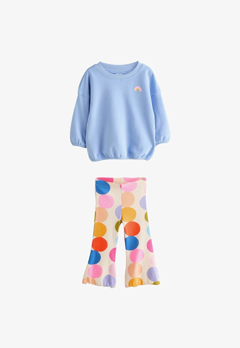 Lichtblauwe sweatshirt met elastische manchetten en een regenboogpatch, gecombineerd met crèmekleurige leggings met multicolore stippen in verschillende maten.