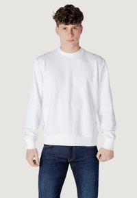 Felpa bianca con collo rotondo, polsini e orlo a coste. Tessuto morbido, vestibilità rilassata, abbinata a jeans blu scuro, design minimale.