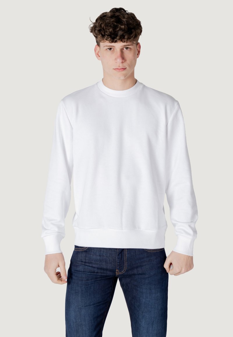 Felpa bianca con collo rotondo, polsini e orlo a coste. Tessuto morbido, vestibilità rilassata, abbinata a jeans blu scuro, design minimale.