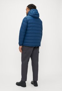Blue puffer jacket with a hood, featuring horizontal quilting and a fitted silhouette. Paired with dark cargo pants and black boots.