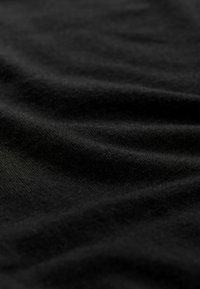 Čierna bavlnená látka s hladkou textúrou, zobrazujúca jemné záhyby a pokrčenia, ktoré zdôrazňujú jej mäkkosť a splývavosť. Bez vzorov alebo dekoratívnych prvkov.