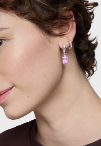 Boucle d'oreille en argent avec un pendentif en forme d'ours rose. Le pendentif présente une finition brillante et des détails ronds, fixé par une chaîne fine.