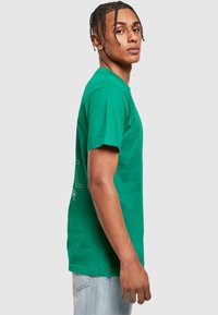 Green cotton t-shirt with short sleeves, crew neck, and printed design on the front. Soft texture and regular fit, displayed from the side.
