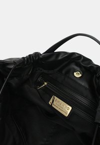 Interno di una borsa a tracolla in pelle nera con texture liscia, con una tasca con zip e hardware dorato con marchio. Design con chiusura a coulisse.