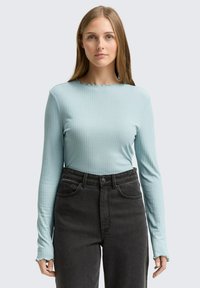 Ljusblå långärmad skjorta med ribbad textur och scalloped halsringning, kombinerad med högmidjade svarta jeans.
