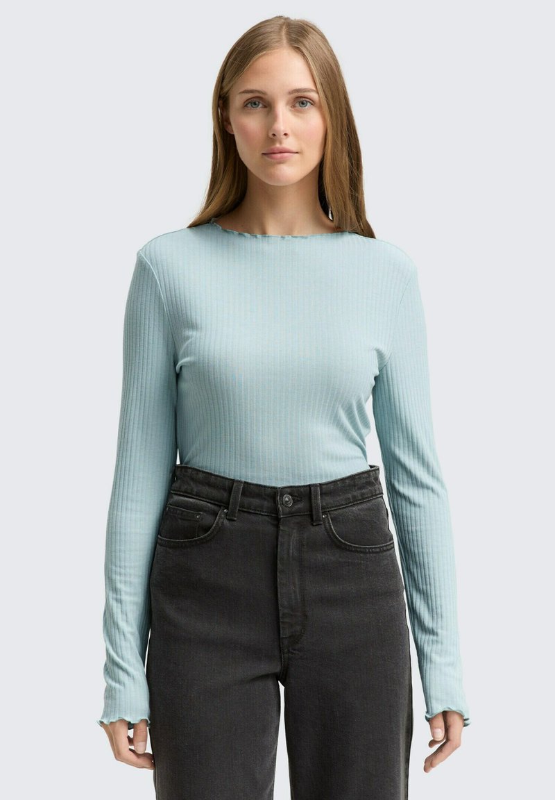 Ljusblå långärmad skjorta med ribbad textur och scalloped halsringning, kombinerad med högmidjade svarta jeans.