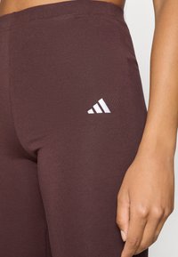 Leggings bordôs feitos de material elástico, com um logo branco da Adidas na lateral, design justo e textura suave.