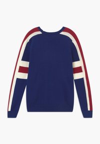 Niebieski sweter robiony na drutach z czerwono-białymi paskami na ramionach. Posiada okrągły dekolt oraz ściągacze przy rękawach i u dołu.