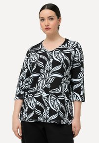 Černý top s bílým vzorem listů, výstřih do V a tříčtvrtečními rukávy. Vyrobeno z měkkého, elastického materiálu.