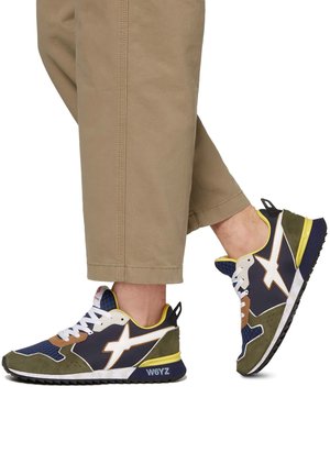 Sneaker sportive con una combinazione di materiali blu navy, olive e beige, caratterizzati da un logo bianco, dettagli testurizzati e una suola in gomma con rifiniture gialle.