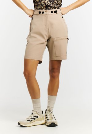 Benen met beige knielange cargoshorts met zijzakken, beige sokken en beige-zwart sportieve schoenen op een witte achtergrond.