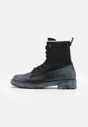 Botte de combat noire à lacets avec bas en cuir mat, dessus en tissu, et languette de traction à l'arrière, vue de profil sur fond blanc.