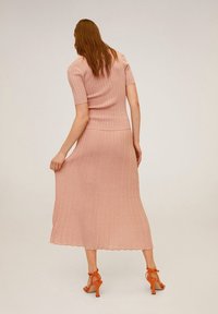 Vestido de punto de manga corta en rosa pastel, con un corsé ajustado y un dobladillo acampanado con forma de concha. Combinado con sandalias de tacón naranjas.