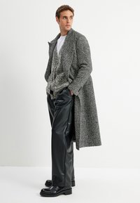 Lungo cappotto grigio a zigzag su un cardigan grigio testurizzato, abbinato a pantaloni in pelle nera lucida e stivali in pelle nera.