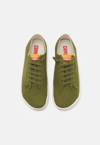 Grüne Leinenschuhe mit weißen Gummisohlen, ausgestattet mit sechs Ösen, runder Zehenform und Camper-Branding auf der Zunge.