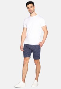 T-shirt blanc à col rond et short à cordon de serrage bleu marine avec un motif texturé, associé à des baskets blanches.