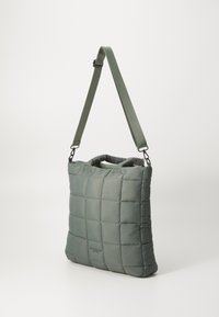 Sac à épaule matelassé vert avec une texture rembourrée, design plat et poignées courtes ; comprend une sangle ajustable et amovible pour plus de polyvalence.