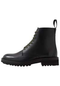 Botte chelsea en cuir noir avec des lacets verts, bout rond, tirette à l'arrière et semelle robuste pour l'adhérence. Texture de surface lisse.
