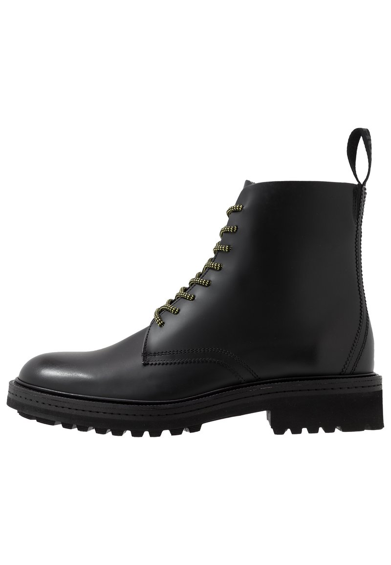 Botte chelsea en cuir noir avec des lacets verts, bout rond, tirette à l'arrière et semelle robuste pour l'adhérence. Texture de surface lisse.