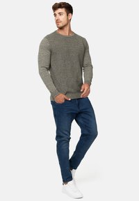 Grå struktureret sweater med et ribbet vandret design, kombineret med mørkeblå jeans og hvide sneakers. Afslappet pasform og rene linjer.