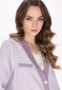 Lavendelfärgad tweedblazer med en kontrasterande krage, texturerad tygkvalitet och en liten fickdetalj. Bärs över en krämfärgad topp med spetsdetaljer.