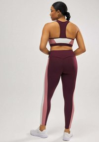 Sujetador deportivo burdeos y leggins con paneles laterales blancos y rosas. La tela se ajusta al cuerpo con una textura suave y un diseño de cinturilla curvada.