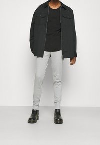 Czarna koszula zapinana na zamek, czarny t-shirt, szare obcisłe spodnie i czarne botki za kostkę. Kluczowe cechy to kieszenie i gładka faktura materiału.