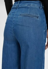 Blue denim jeans featuring a relaxed fit, detailed stitching, and two back pockets with horizontal openings. Soft texture and mid-rise design.