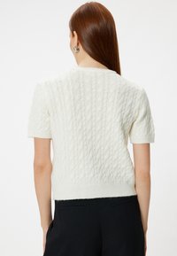 Jersey de punto en crema con un patrón de trenzas, con mangas cortas y un ajuste corto. Fabricado en un suave tejido texturizado con un dobladillo acanalado.