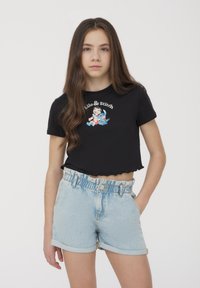 T-shirt nero cropped con grafica di Lilo & Stitch e orlo scallop, abbinato a pantaloni corti in denim blu chiaro con vita elasticizzata.