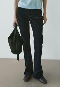 Pantaloni a zampa in velluto a coste scuro abbinati a un top corto azzurro e una borsa in suede nera. Mocassini marroni completano il look.