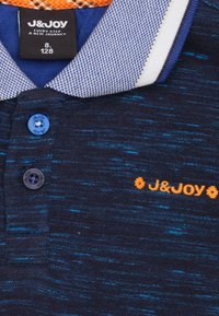 Polo shirt bleu marine en tissu texturé, avec un col à motifs, broderie de logo orange et boutons bleus.